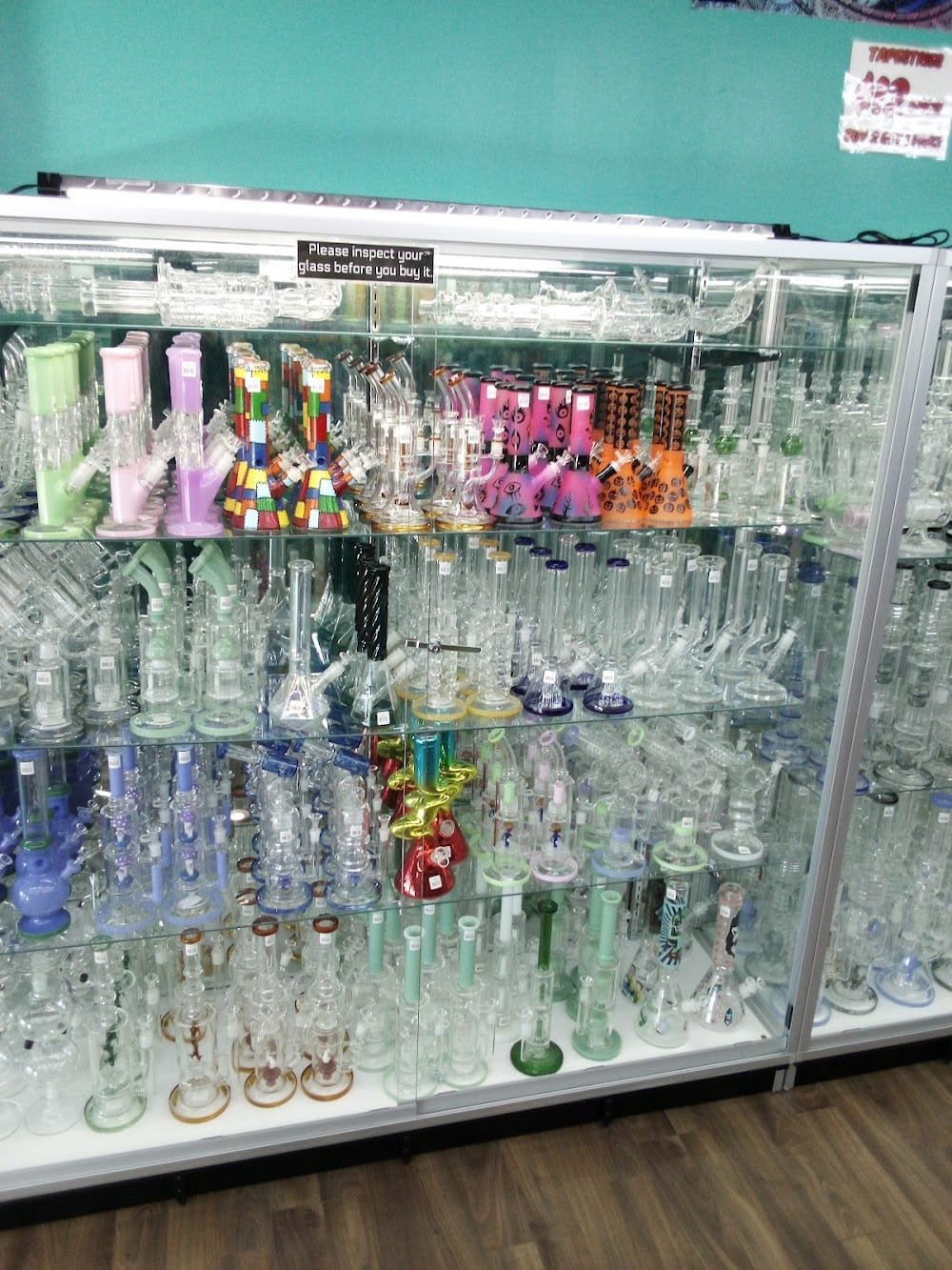 Full glass display wall with hundreds of water pipes, bongs, and bubblers in clear, pink, blue, green and multicolor styles